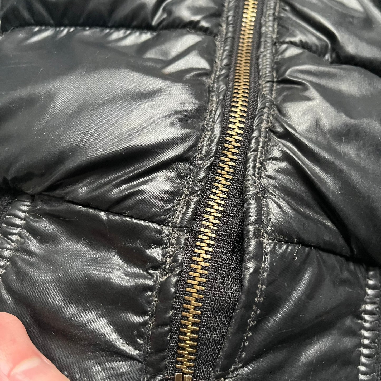 Philipp Plein 2010s Black Waxed Puffer Jacket is a black puffer jacket with a removable fur-trimmed hood attached by zipper. The jacket features heavy silver-tone hardware throughout, including large zipper pulls shaped as crosses with a skull in the center, used on the front pockets and chest pockets. The right chest has a black “P” patch set with crystals, while the left chest features two zip pockets. The hood drawstrings are finished with silver skull tips marked with a “P.”

Both shoulders are finished