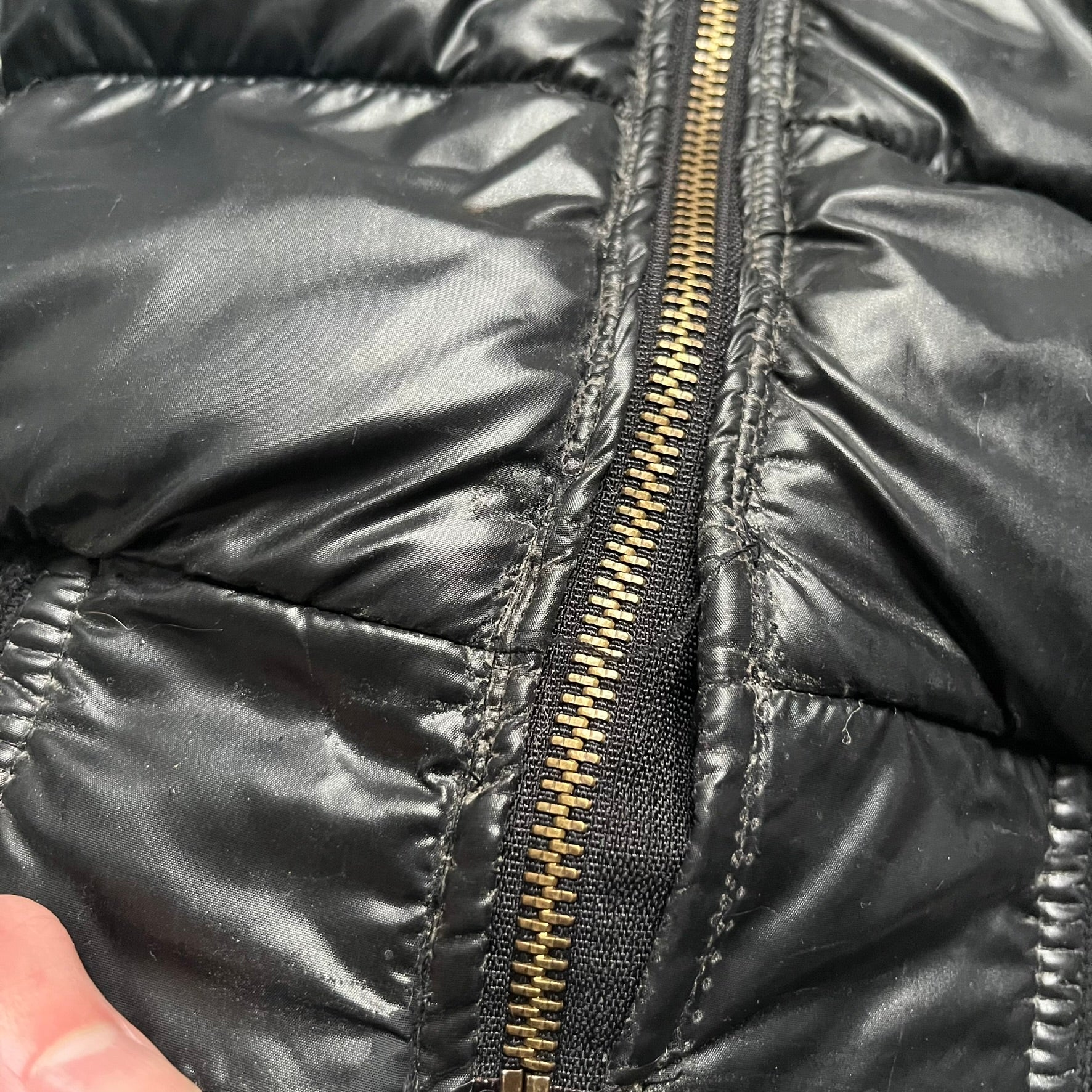 Philipp Plein 2010s Black Waxed Puffer Jacket is a black puffer jacket with a removable fur-trimmed hood attached by zipper. The jacket features heavy silver-tone hardware throughout, including large zipper pulls shaped as crosses with a skull in the center, used on the front pockets and chest pockets. The right chest has a black “P” patch set with crystals, while the left chest features two zip pockets. The hood drawstrings are finished with silver skull tips marked with a “P.”

Both shoulders are finished