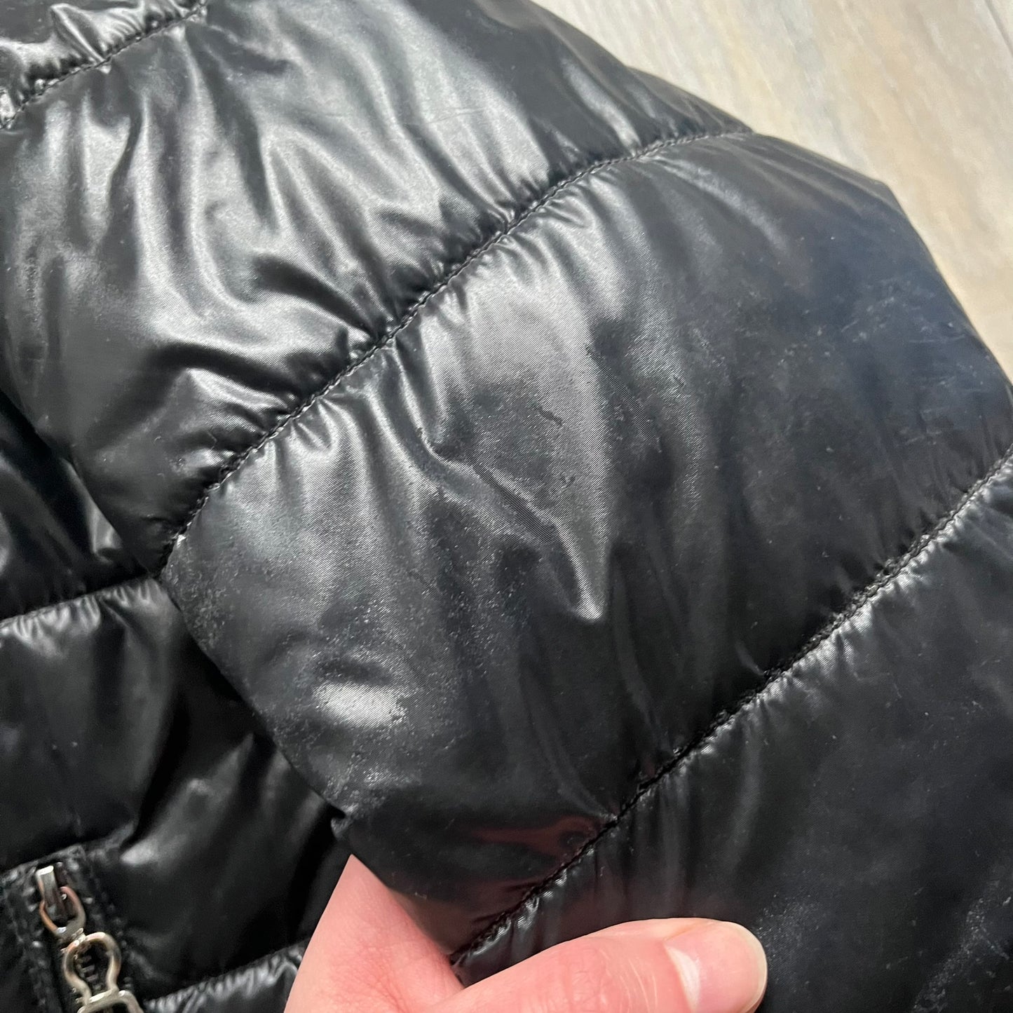 Philipp Plein 2010s Black Waxed Puffer Jacket is a black puffer jacket with a removable fur-trimmed hood attached by zipper. The jacket features heavy silver-tone hardware throughout, including large zipper pulls shaped as crosses with a skull in the center, used on the front pockets and chest pockets. The right chest has a black “P” patch set with crystals, while the left chest features two zip pockets. The hood drawstrings are finished with silver skull tips marked with a “P.”

Both shoulders are finished
