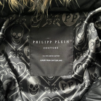 Philipp Plein 2010s Black Waxed Puffer Jacket is a black puffer jacket with a removable fur-trimmed hood attached by zipper. The jacket features heavy silver-tone hardware throughout, including large zipper pulls shaped as crosses with a skull in the center, used on the front pockets and chest pockets. The right chest has a black “P” patch set with crystals, while the left chest features two zip pockets. The hood drawstrings are finished with silver skull tips marked with a “P.”

Both shoulders are finished