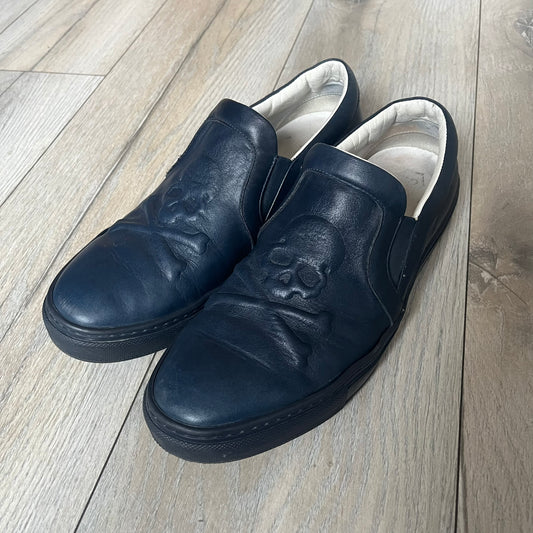 Philipp Plein Navy Skull Slip-Ons are dark navy slip-on sneakers with white interior lining. The front features large raised skull logos, while the sole side displays the Philipp Plein text/logo. Made in Italy, the interior includes an authentic PP tag.