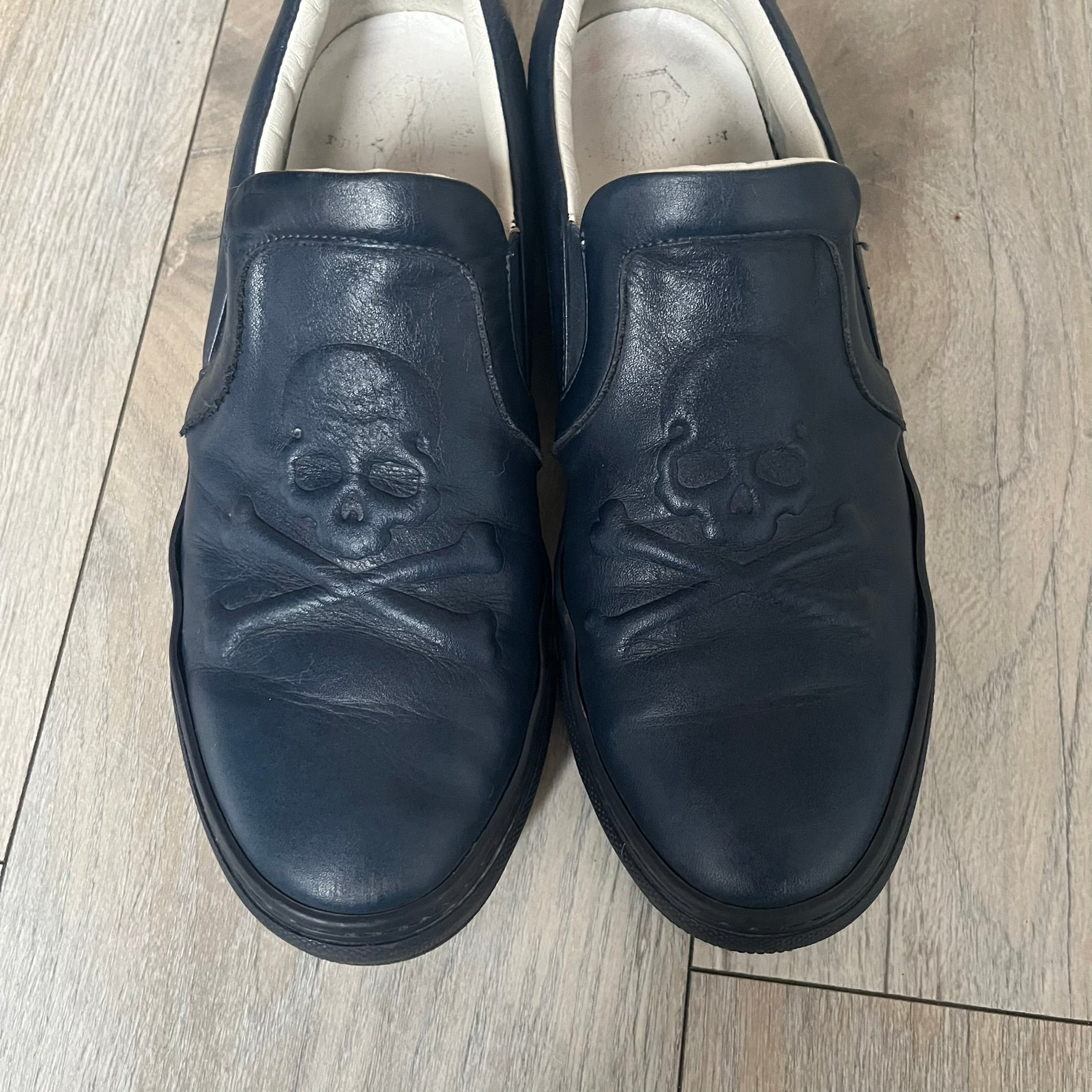 Philipp Plein Navy Skull Slip-Ons are dark navy slip-on sneakers with white interior lining. The front features large raised skull logos, while the sole side displays the Philipp Plein text/logo. Made in Italy, the interior includes an authentic PP tag.