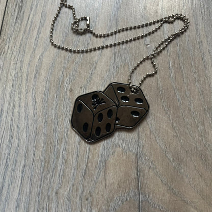 Philipp Plein Two Dices Necklace features a flat metal pendant from Philipp Plein paired with a non-original ball chain. The pendant is designed as two connected dice in a dark grey finish with black enamel dots, with one side replacing the dots with the Philipp Plein skull motif, while the reverse is engraved with the brand logo. Originally used as a zipper pull or accessory attachment, the piece is made in Italy and comes from the 2013 “Hardcore Diamonds” collection.