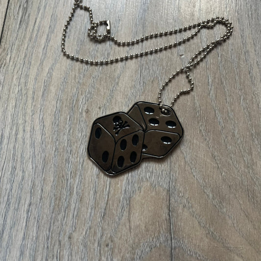 Philipp Plein Two Dices Necklace features a flat metal pendant from Philipp Plein paired with a non-original ball chain. The pendant is designed as two connected dice in a dark grey finish with black enamel dots, with one side replacing the dots with the Philipp Plein skull motif, while the reverse is engraved with the brand logo. Originally used as a zipper pull or accessory attachment, the piece is made in Italy and comes from the 2013 “Hardcore Diamonds” collection.