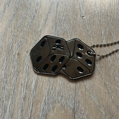 Philipp Plein Two Dices Necklace features a flat metal pendant from Philipp Plein paired with a non-original ball chain. The pendant is designed as two connected dice in a dark grey finish with black enamel dots, with one side replacing the dots with the Philipp Plein skull motif, while the reverse is engraved with the brand logo. Originally used as a zipper pull or accessory attachment, the piece is made in Italy and comes from the 2013 “Hardcore Diamonds” collection.