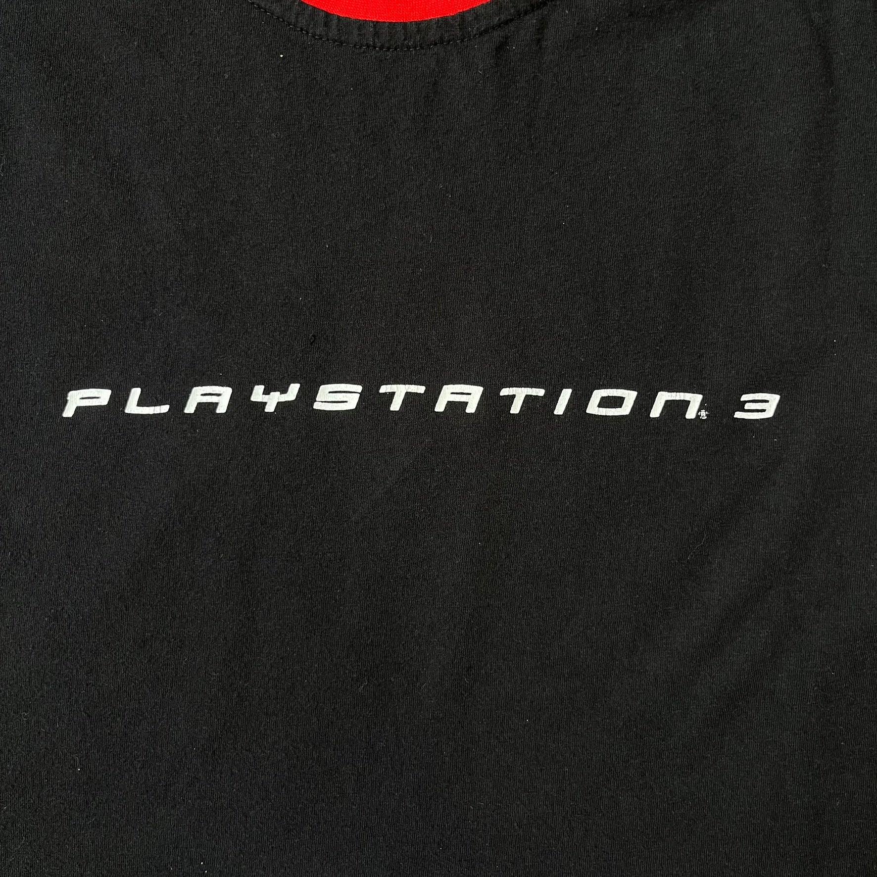 PlayStation 3 Game Mania Crew 2000s Longsleeve is a black long-sleeve shirt featuring red collar and shoulder stripe detailing running along the tops of the sleeves. The front displays a white PlayStation 3 logo, while the back is printed with the "Game Mania" logo above "CREW" lettering. Finished with distinctive yellow Game Mania neck tag, this event/store-exclusive piece was produced for Game Mania staff and promotional use.