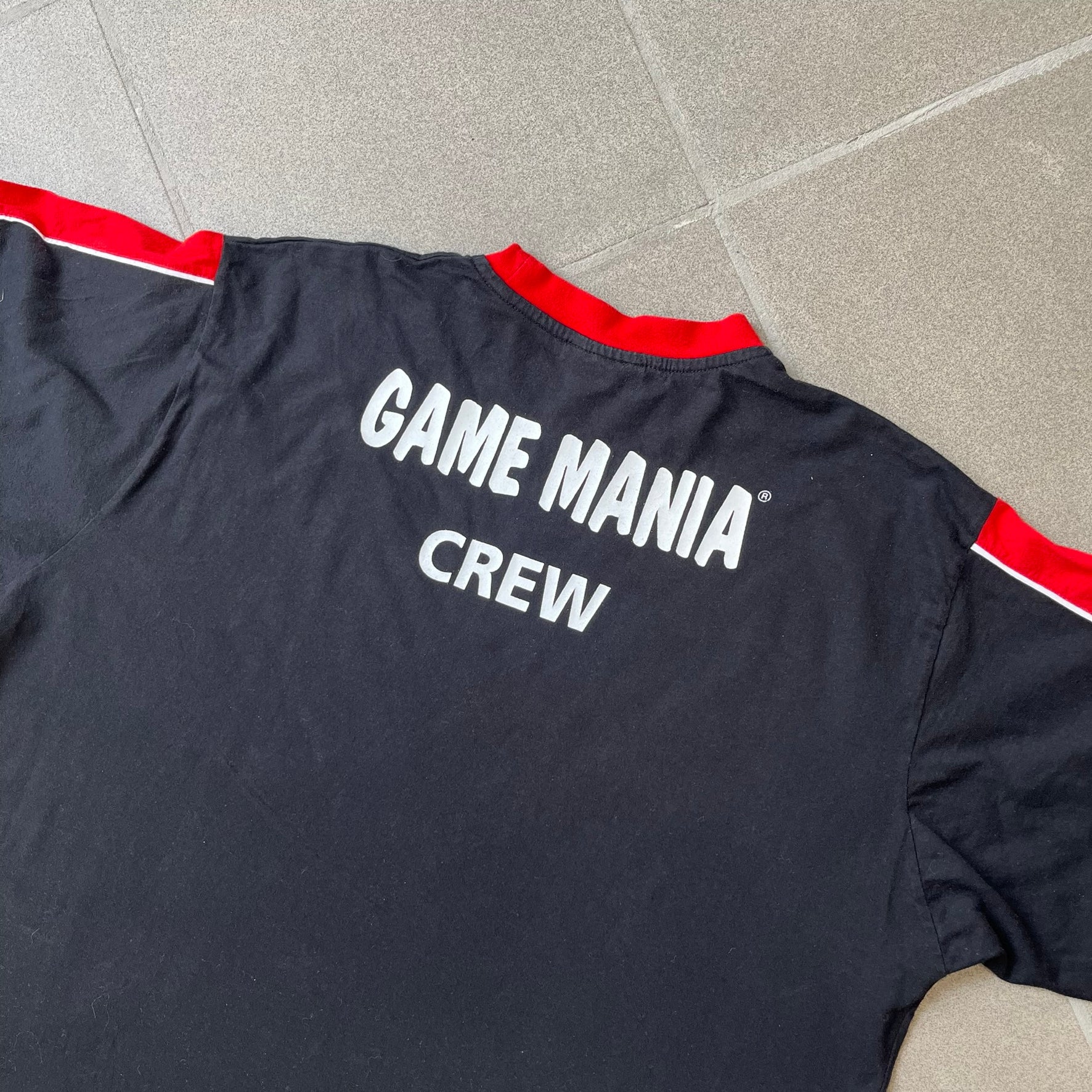 PlayStation 3 Game Mania Crew 2000s Longsleeve is a black long-sleeve shirt featuring red collar and shoulder stripe detailing running along the tops of the sleeves. The front displays a white PlayStation 3 logo, while the back is printed with the "Game Mania" logo above "CREW" lettering. Finished with distinctive yellow Game Mania neck tag, this event/store-exclusive piece was produced for Game Mania staff and promotional use.