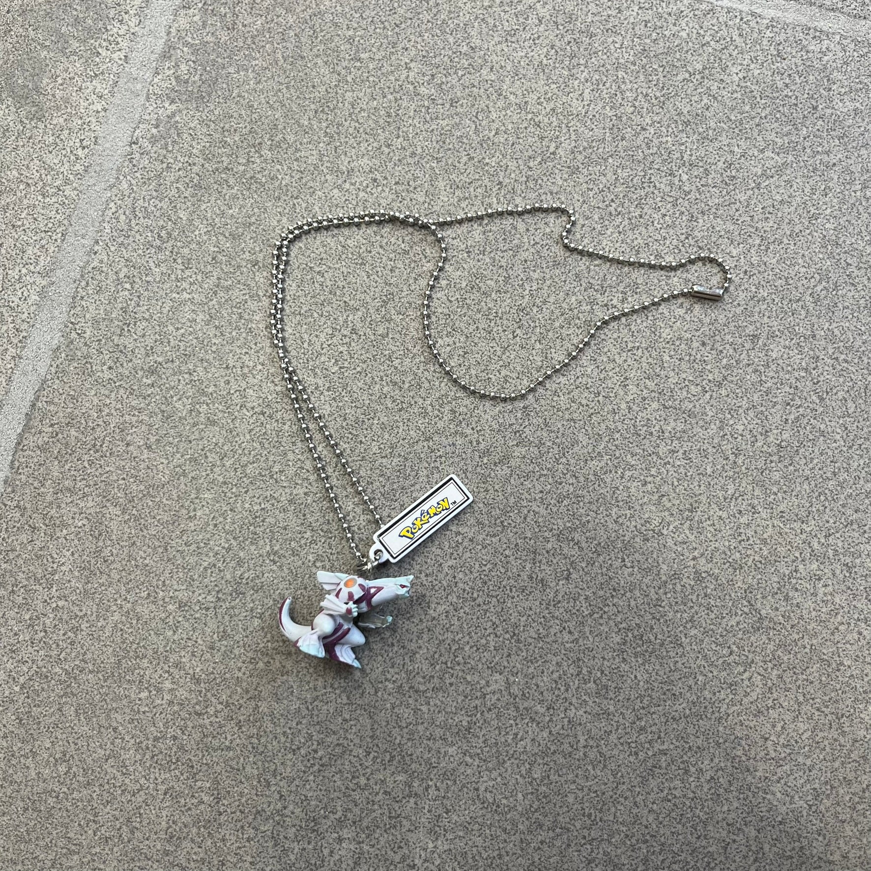 Pokémon 2008 Palkia Necklace is a converted Palkia key chain turned into a wearable pendant. It features a small 3D Palkia figure from the Pokémon franchise with an attached Pokémon tag containing licensing details on the back. The pendant design comes from a 2008 key chain release.