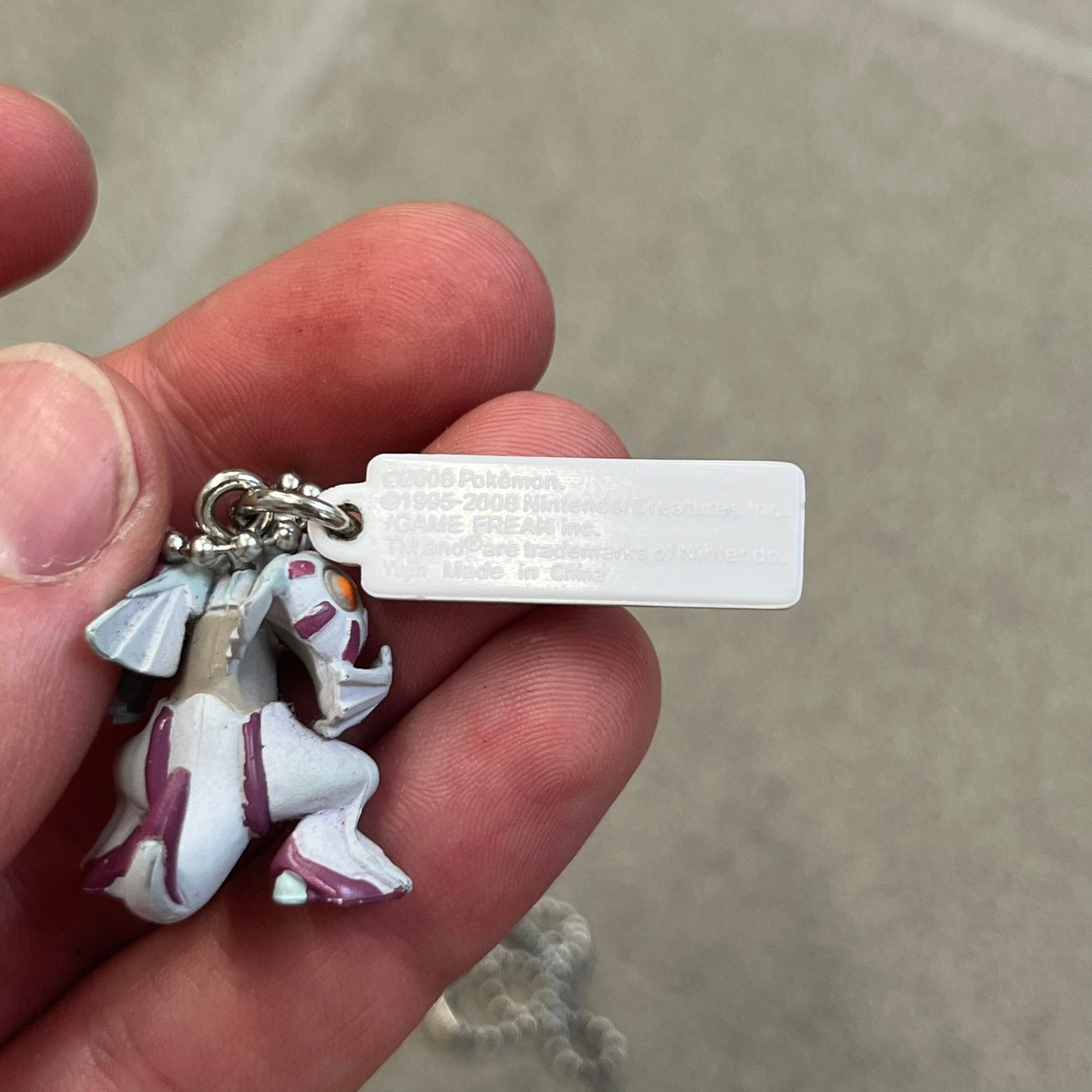 Pokémon 2008 Palkia Necklace is a converted Palkia key chain turned into a wearable pendant. It features a small 3D Palkia figure from the Pokémon franchise with an attached Pokémon tag containing licensing details on the back. The pendant design comes from a 2008 key chain release.