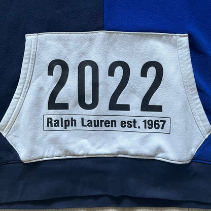 Polo Ralph Lauren x Fortnite 2022 Hoodie featuring a two-tone split design in blue and navy with a white hood. The front showcases a large white panel with “2022” text, Ralph Lauren Est. 1967 branding, and a Fortnite logo, along with an oversized embroidered Polo logo above. A limited collaboration piece combining Ralph Lauren’s heritage aesthetic with Fortnite’s playful edge.