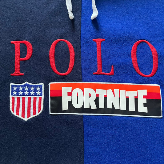 Polo Ralph Lauren x Fortnite 2022 Hoodie featuring a two-tone split design in blue and navy with a white hood. The front showcases a large white panel with “2022” text, Ralph Lauren Est. 1967 branding, and a Fortnite logo, along with an oversized embroidered Polo logo above. A limited collaboration piece combining Ralph Lauren’s heritage aesthetic with Fortnite’s playful edge.