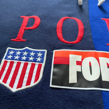 Polo Ralph Lauren x Fortnite 2022 Hoodie featuring a two-tone split design in blue and navy with a white hood. The front showcases a large white panel with “2022” text, Ralph Lauren Est. 1967 branding, and a Fortnite logo, along with an oversized embroidered Polo logo above. A limited collaboration piece combining Ralph Lauren’s heritage aesthetic with Fortnite’s playful edge.