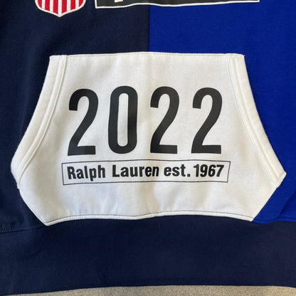 Polo Ralph Lauren x Fortnite 2022 Hoodie featuring a two-tone split design in blue and navy with a white hood. The front showcases a large white panel with “2022” text, Ralph Lauren Est. 1967 branding, and a Fortnite logo, along with an oversized embroidered Polo logo above. A limited collaboration piece with paper tags.