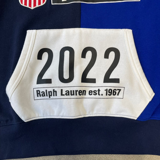 Polo Ralph Lauren x Fortnite 2022 Hoodie featuring a two-tone split design in blue and navy with a white hood. The front showcases a large white panel with “2022” text, Ralph Lauren Est. 1967 branding, and a Fortnite logo, along with an oversized embroidered Polo logo above. A limited collaboration piece with paper tags.