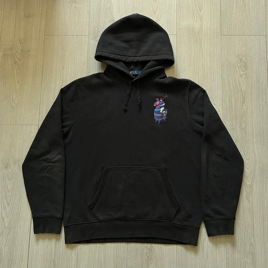  Polo Ralph Lauren x Fortnite black hoodie featuring a detailed embroidered purple Fortnite llama with the RL rider logo placed on top. Made from a 66% cotton and 34% polyester blend, it has a classic pullover construction with an attached hood and front kangaroo pocket. The embroidery is positioned on the left chest and stands out with clean stitching and sharp detail.