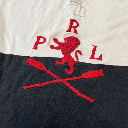 Polo Ralph Lauren Red Lion PRL Rugby Longsleeve features a black and white striped rugby design with four horizontal stripes across the front and additional stripes on the sleeves. The center of the chest has a red embroidered emblem featuring two crossed oars, a lion, and “PRL” lettering above the lion.