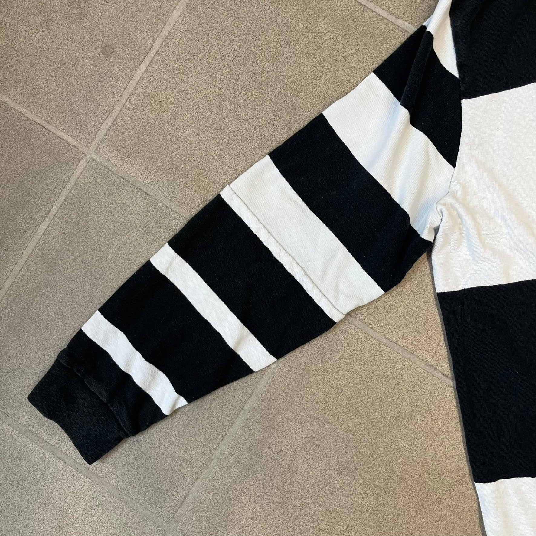 Polo Ralph Lauren Red Lion PRL Rugby Longsleeve features a black and white striped rugby design with four horizontal stripes across the front and additional stripes on the sleeves. The center of the chest has a red embroidered emblem featuring two crossed oars, a lion, and “PRL” lettering above the lion.
