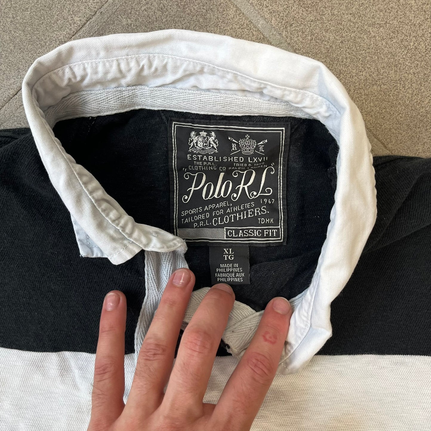Polo Ralph Lauren Red Lion PRL Rugby Longsleeve features a black and white striped rugby design with four horizontal stripes across the front and additional stripes on the sleeves. The center of the chest has a red embroidered emblem featuring two crossed oars, a lion, and “PRL” lettering above the lion.