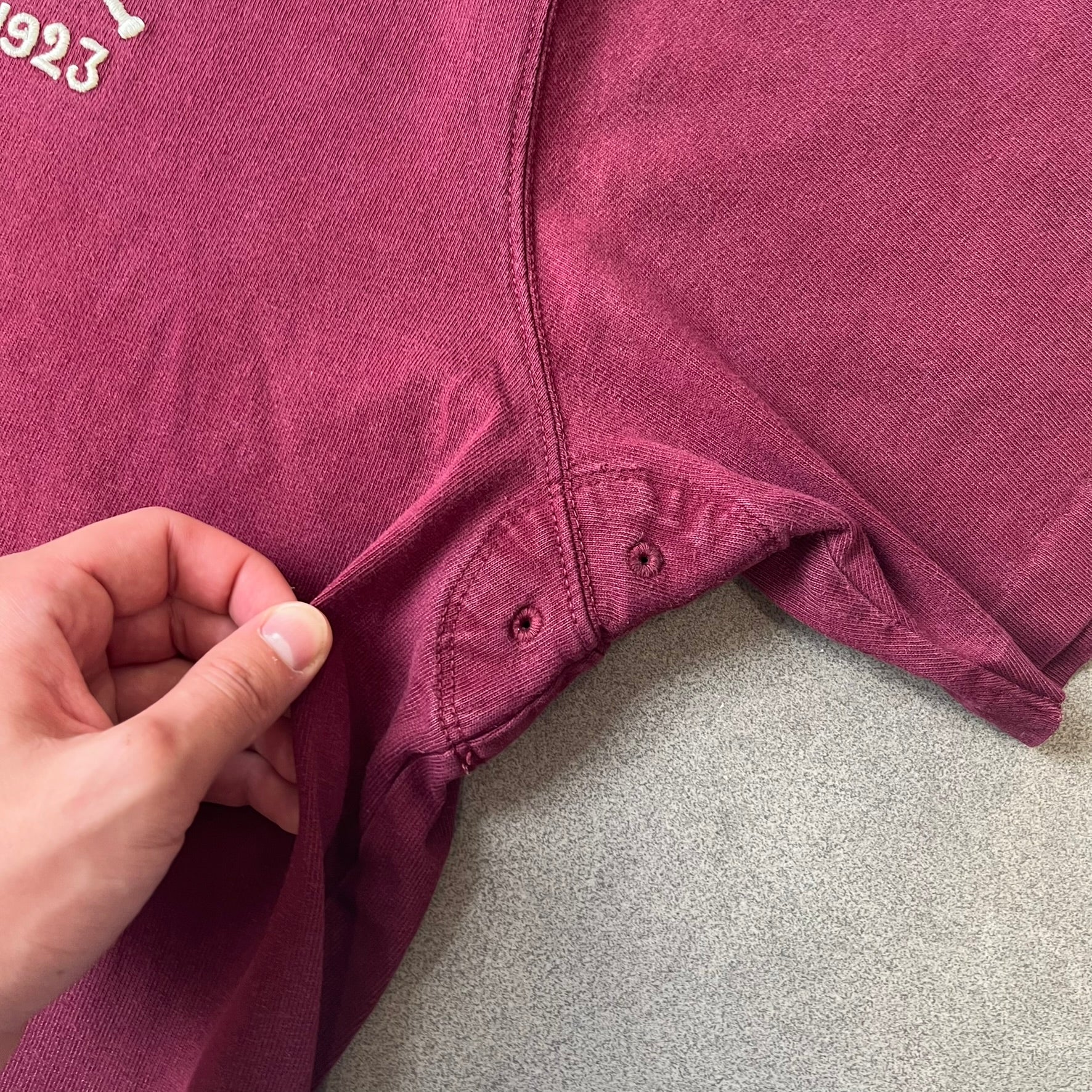 Polo Ralph Lauren “Skull &amp; Crossbone” Rugby Polo is a burgundy short-sleeve polo made from 100% cotton. It features a white contrasting rugby-style collar and a three-button placket. On the chest is a white embroidered skull and crossbones design with “1923” below it and “R.L.F.C” above. The design includes a split hem and embroidered detailing on the front.