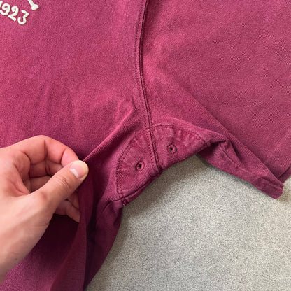 Polo Ralph Lauren “Skull &amp; Crossbone” Rugby Polo is a burgundy short-sleeve polo made from 100% cotton. It features a white contrasting rugby-style collar and a three-button placket. On the chest is a white embroidered skull and crossbones design with “1923” below it and “R.L.F.C” above. The design includes a split hem and embroidered detailing on the front.
