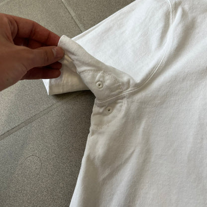 Polo Ralph Lauren “Skull &amp; Crossbone” Rugby Polo is a white short-sleeve polo made from 100% cotton. It features a black contrasting rugby-style collar and a three-button placket. On the chest is a black embroidered skull and crossbones design with “1923” below it and “R.L.F.C” above. The design includes a split hem and embroidered detailing on the front.