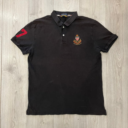 Polo Ralph Lauren ’67 Crest Polo in dark brown. Features an embroidered crest on the left chest with “1967” detail and a big red “67” patch on the sleeve. Classic cotton polo construction with short sleeves and ribbed collar.