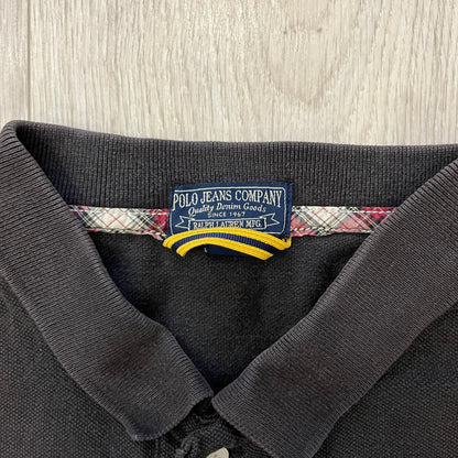 Polo Ralph Lauren ’67 Crest Polo in dark brown. Features an embroidered crest on the left chest with “1967” detail and a big red “67” patch on the sleeve. Classic cotton polo construction with short sleeves and ribbed collar.