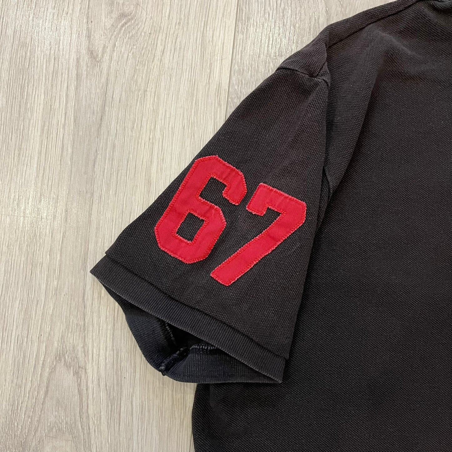 Polo Ralph Lauren ’67 Crest Polo in dark brown. Features an embroidered crest on the left chest with “1967” detail and a big red “67” patch on the sleeve. Classic cotton polo construction with short sleeves and ribbed collar.