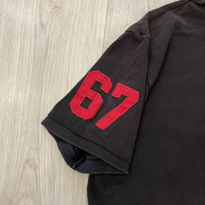 Polo Ralph Lauren ’67 Crest Polo in dark brown. Features an embroidered crest on the left chest with “1967” detail and a big red “67” patch on the sleeve. Classic cotton polo construction with short sleeves and ribbed collar.