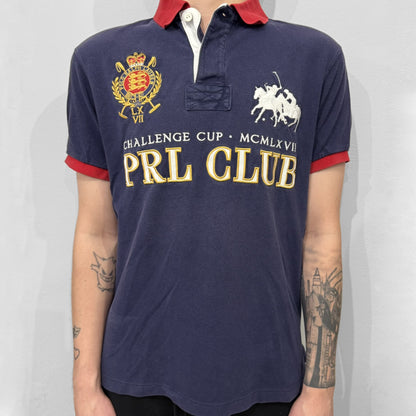 Ralph Lauren’s “PRL Club” Big Pony Polo stands out with detailed front embroidery, combining a Big Pony motif, Challenge Cup text, and a large crest. The navy body is paired with red accents on the collar and sleeves, with a signature oversized “3” and PRL Club branding on the back.