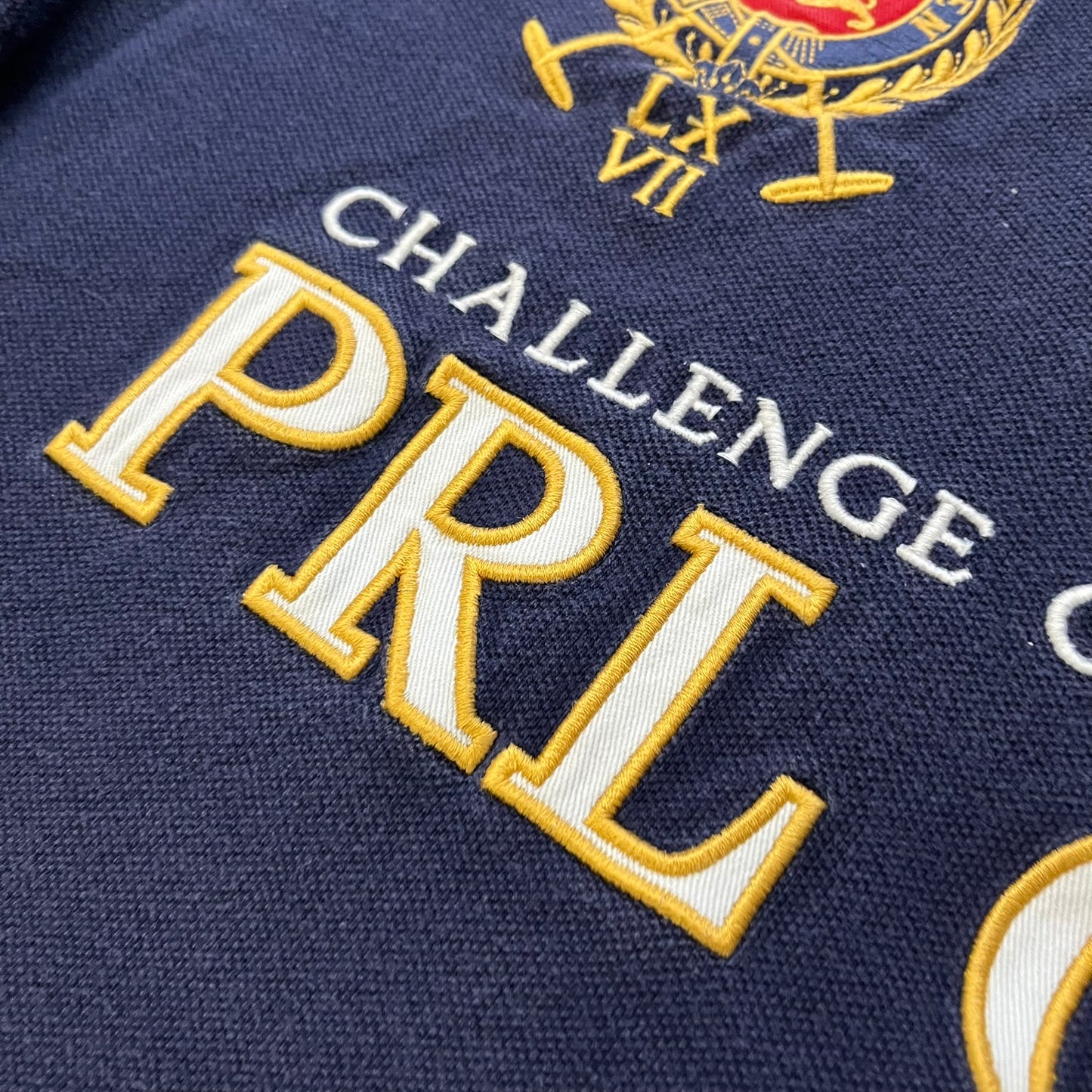 Ralph Lauren’s “PRL Club” Big Pony Polo stands out with detailed front embroidery, combining a Big Pony motif, Challenge Cup text, and a large crest. The navy body is paired with red accents on the collar and sleeves, with a signature oversized “3” and PRL Club branding on the back.