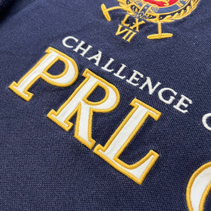 Ralph Lauren’s “PRL Club” Big Pony Polo stands out with detailed front embroidery, combining a Big Pony motif, Challenge Cup text, and a large crest. The navy body is paired with red accents on the collar and sleeves, with a signature oversized “3” and PRL Club branding on the back.
