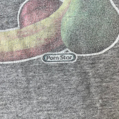 Porn Star Clothing 90's Fruits Gray Tee features a grey T-shirt with an apple, banana, and pear graphic on the chest, arranged as a you know what. A small Porn Star logo is printed underneath, with the “Good Clothing for Bad People” branding on the neck tag. The shirt has two professionally repaired holes under the armpits.
