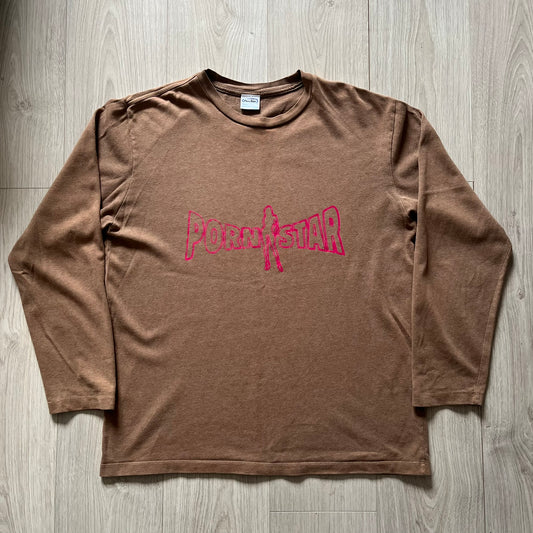 Vintage 90’s Porn Star Clothing longsleeve in brown, featuring a bold pink logo on the chest with a silhouette outline of a woman between the words “Porn” and “Star.” Crafted with quality construction, it carries the brand’s signature edgy aesthetic. Finished with a playful “must be 18 or over” detail on the tag, this rare piece embodies 90’s streetwear provocative style.