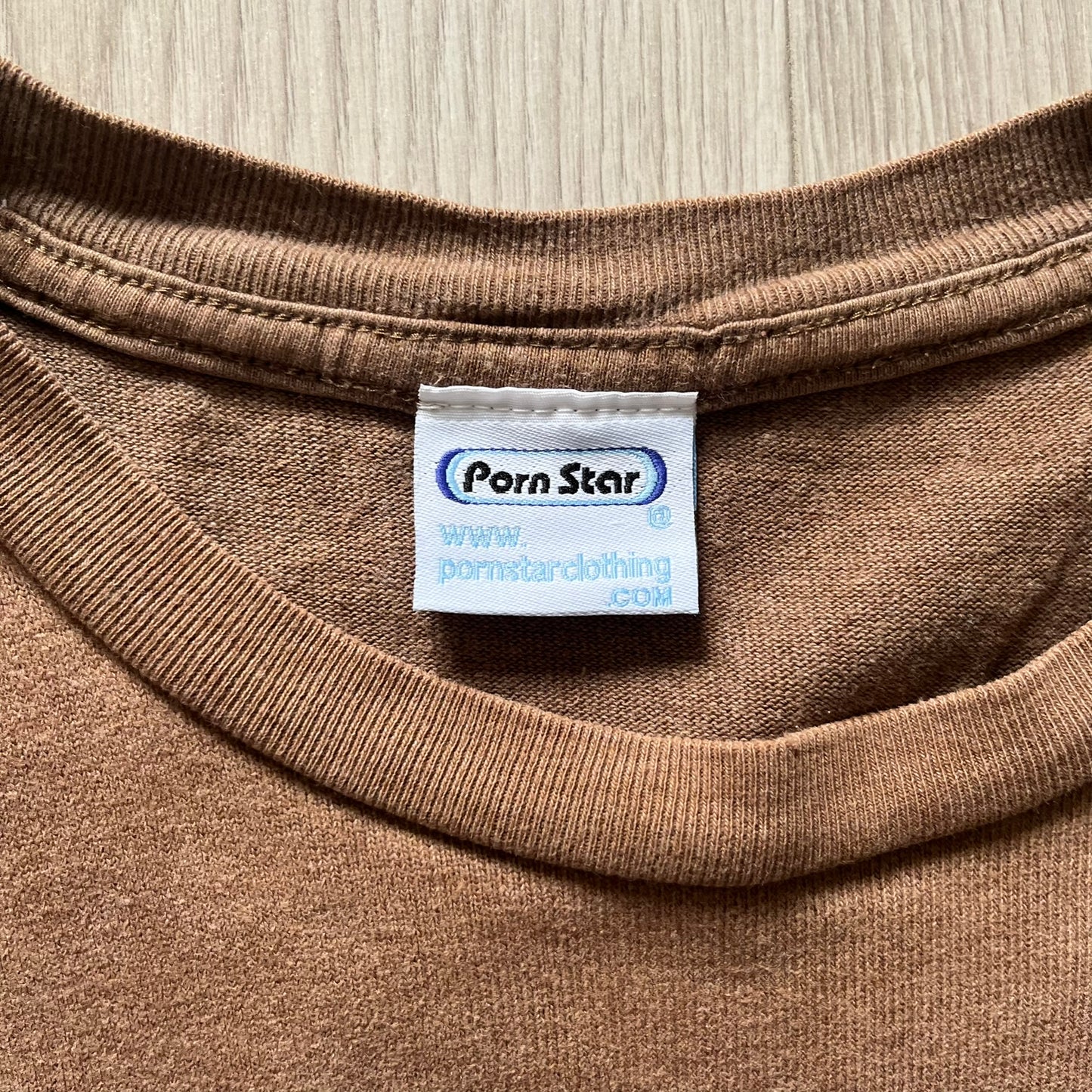 Vintage 90’s Porn Star Clothing longsleeve in brown, featuring a bold pink logo on the chest with a silhouette outline of a woman between the words “Porn” and “Star.” Crafted with quality construction, it carries the brand’s signature edgy aesthetic. Finished with a playful “must be 18 or over” detail on the tag, this rare piece embodies 90’s streetwear provocative style.