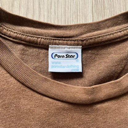 Vintage 90’s Porn Star Clothing longsleeve in brown, featuring a bold pink logo on the chest with a silhouette outline of a woman between the words “Porn” and “Star.” Crafted with quality construction, it carries the brand’s signature edgy aesthetic. Finished with a playful “must be 18 or over” detail on the tag, this rare piece embodies 90’s streetwear provocative style.