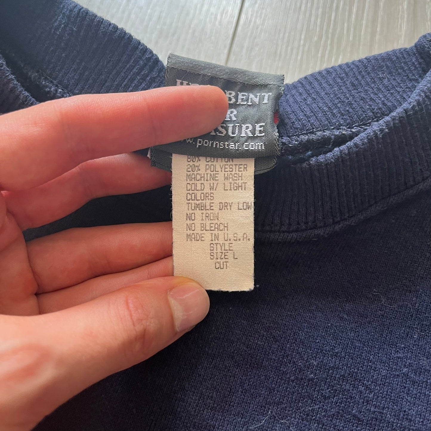 Hand holding a clothing tag on a navy blue garment with a blurred background