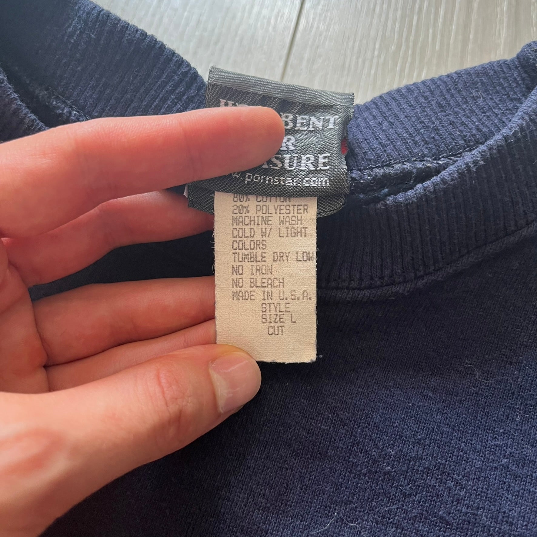 Hand holding a clothing tag on a navy blue garment with a blurred background