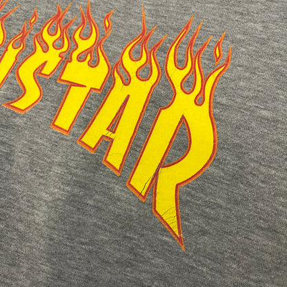 Porn Star Clothing Thrasher Hoodie from the 1990s, made in a gray cotton fabric. The front features a large flame-style “Pornstar” logo that is a spin-off of the Trasher one, with matching flame graphics running down both sleeves. Designed with an adjustable drawstring hood, front kangaroo pocket, and ribbed cuffs and hem. Finished with the original “Must Be 18 Or Over” Porn Star Clothing tag.