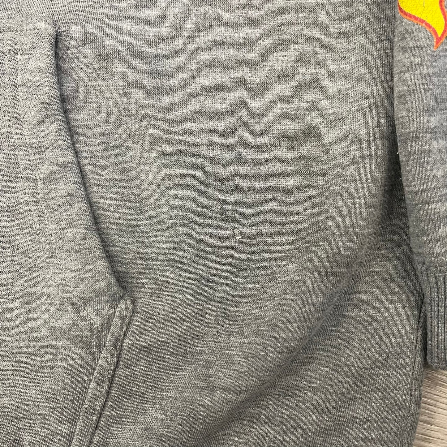 Porn Star Clothing Thrasher Hoodie from the 1990s, made in a gray cotton fabric. The front features a large flame-style “Pornstar” logo that is a spin-off of the Trasher one, with matching flame graphics running down both sleeves. Designed with an adjustable drawstring hood, front kangaroo pocket, and ribbed cuffs and hem. Finished with the original “Must Be 18 Or Over” Porn Star Clothing tag.