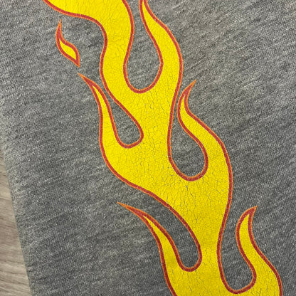 Porn Star Clothing Thrasher Hoodie from the 1990s, made in a gray cotton fabric. The front features a large flame-style “Pornstar” logo that is a spin-off of the Trasher one, with matching flame graphics running down both sleeves. Designed with an adjustable drawstring hood, front kangaroo pocket, and ribbed cuffs and hem. Finished with the original “Must Be 18 Or Over” Porn Star Clothing tag.