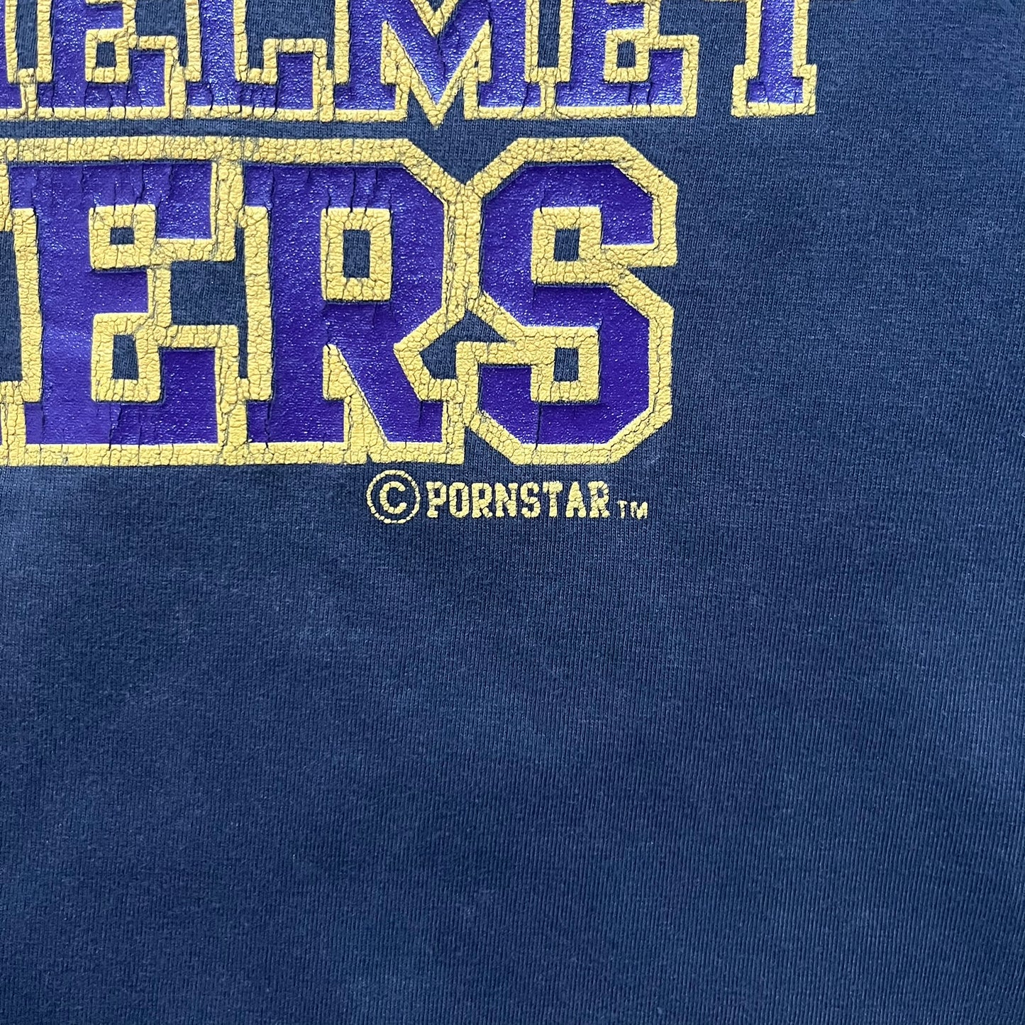 Black T-shirt with a purple football helmet graphic featuring a “P” letter. “Porn Star” text above the helmet in purple with a yellow outline, and “Helmet Packers” text below in purple with a yellow outline. Includes a small Porn Star copyright logo. Vintage piece.