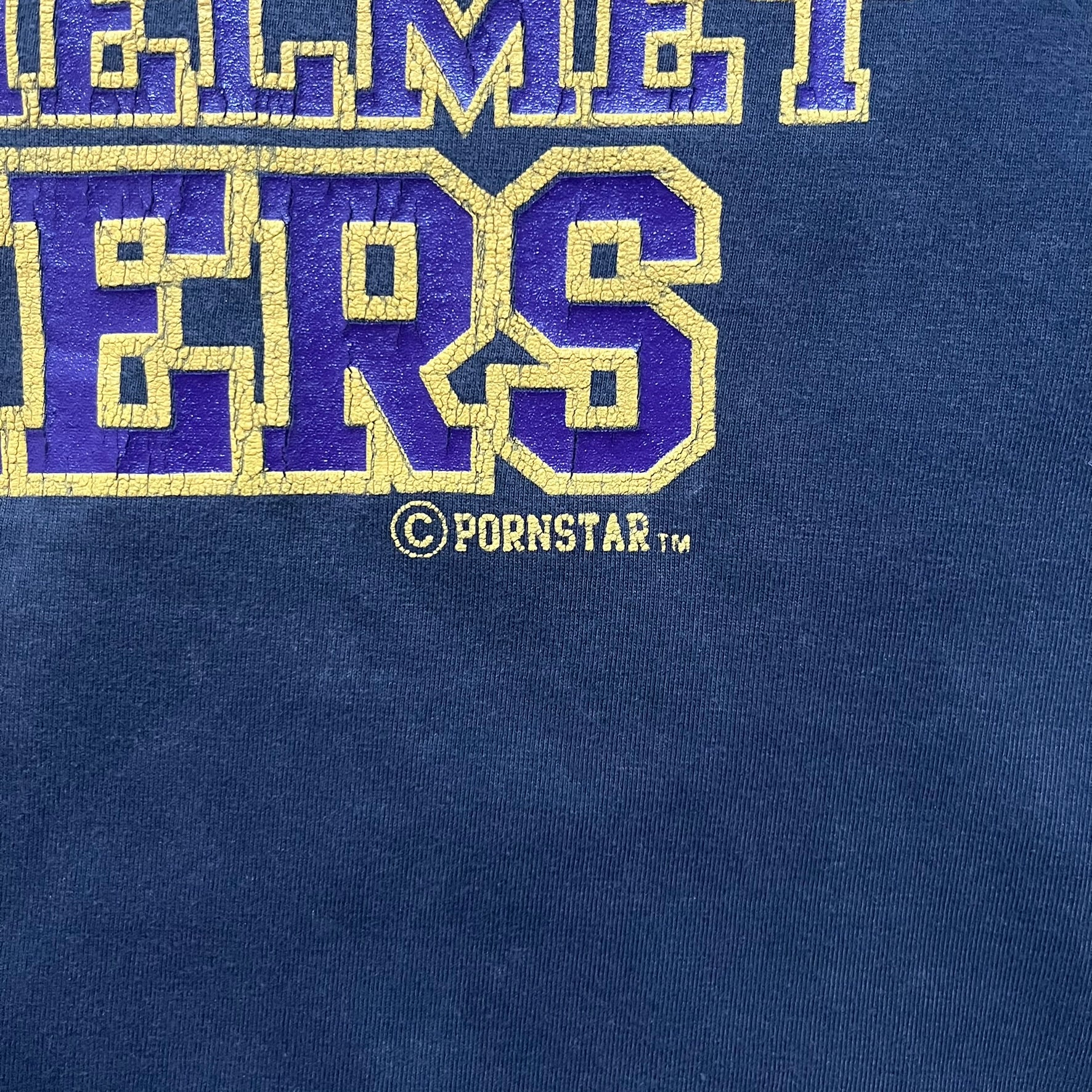 Black T-shirt with a purple football helmet graphic featuring a “P” letter. “Porn Star” text above the helmet in purple with a yellow outline, and “Helmet Packers” text below in purple with a yellow outline. Includes a small Porn Star copyright logo. Vintage piece.