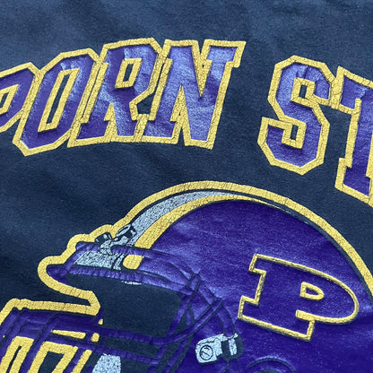 Black T-shirt with a purple football helmet graphic featuring a “P” letter. “Porn Star” text above the helmet in purple with a yellow outline, and “Helmet Packers” text below in purple with a yellow outline. Includes a small Porn Star copyright logo. Vintage piece.