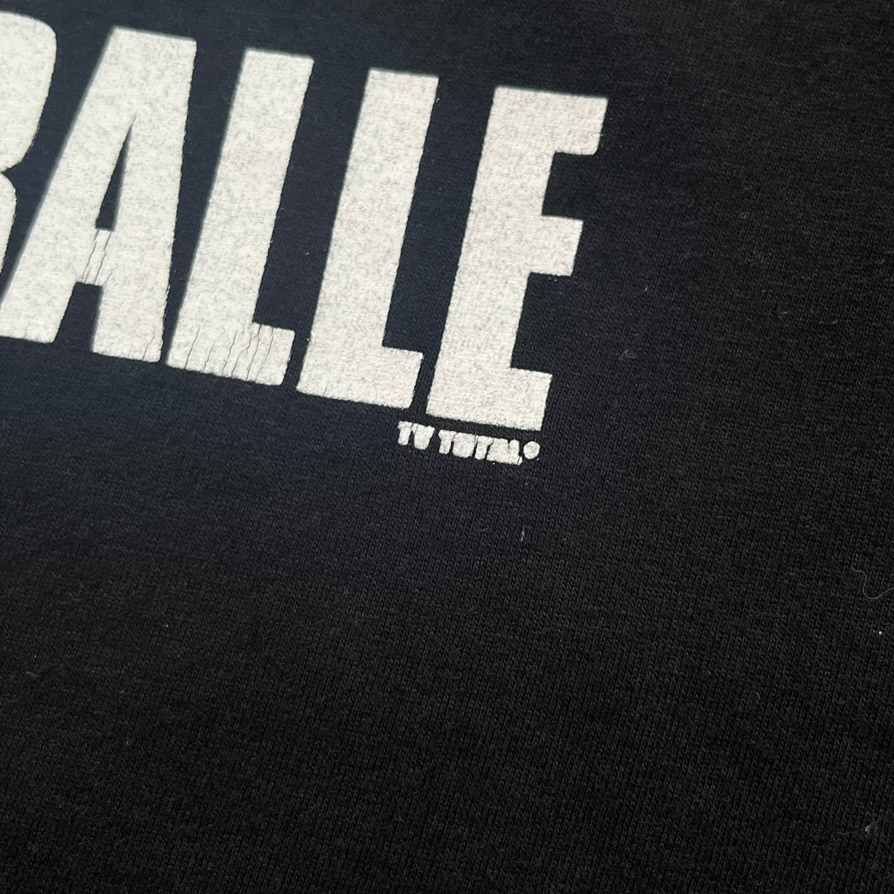 PornoRalle TV 1990s Black Tee is a black short-sleeve T-shirt made on a Jerzees blank. The front features a white PornoRalle logo on the chest with small “TV Total” text beneath. This minimalist design dates from the 1990s.