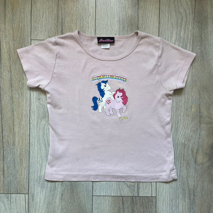 Pornstar Clothing My Little Pony Pink Tee is a women’s baby pink T-shirt featuring a front graphic of two My Little Pony characters under a “My Little Porny” text on a rainbow. A small Pornstar logo sits below the graphic, and the neck tag is black and pink with Pornstar branding. Super rare and hard to find piece.