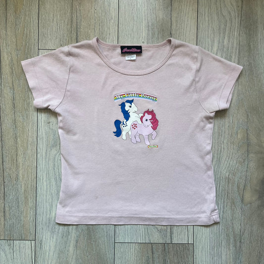 Pornstar Clothing My Little Pony Pink Tee is a women’s baby pink T-shirt featuring a front graphic of two My Little Pony characters under a “My Little Porny” text on a rainbow. A small Pornstar logo sits below the graphic, and the neck tag is black and pink with Pornstar branding. Super rare and hard to find piece.