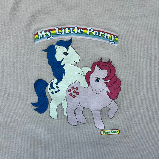 Pornstar Clothing My Little Pony Pink Tee is a women’s baby pink T-shirt featuring a front graphic of two My Little Pony characters under a “My Little Porny” text on a rainbow. A small Pornstar logo sits below the graphic, and the neck tag is black and pink with Pornstar branding. Super rare and hard to find piece.