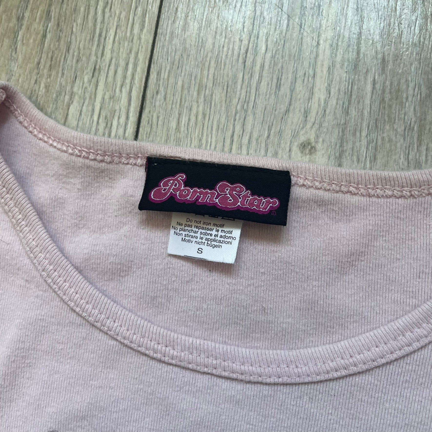 Pornstar Clothing My Little Pony Pink Tee is a women’s baby pink T-shirt featuring a front graphic of two My Little Pony characters under a “My Little Porny” text on a rainbow. A small Pornstar logo sits below the graphic, and the neck tag is black and pink with Pornstar branding. Super rare and hard to find piece.