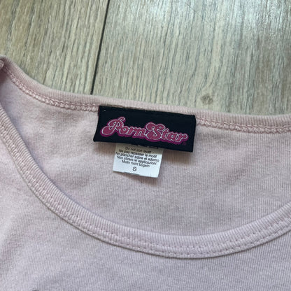 Pornstar Clothing My Little Pony Pink Tee is a women’s baby pink T-shirt featuring a front graphic of two My Little Pony characters under a “My Little Porny” text on a rainbow. A small Pornstar logo sits below the graphic, and the neck tag is black and pink with Pornstar branding. Super rare and hard to find piece.